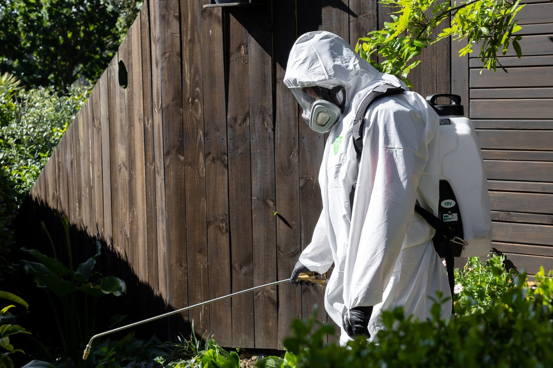A technician treating along a fenceline in full protective equipment